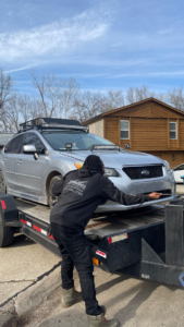 A person securing a silver Subaru onto a flatbed trailer for transport by 82Hauling & More LLC in St. Louis, MO