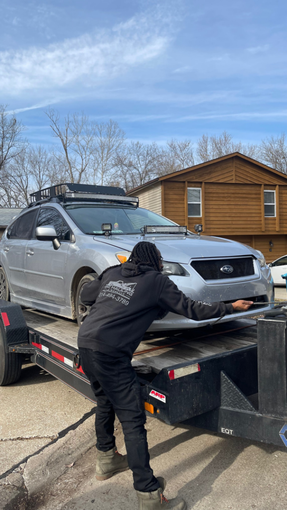 A person securing a silver Subaru onto a flatbed trailer for transport by 82Hauling & More LLC in St. Louis, MO