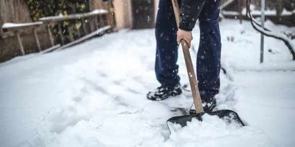 A person actively shoveling snow from a pathway, demonstrating snow removal services by Alex and Sons LLC in Northglenn, CO.