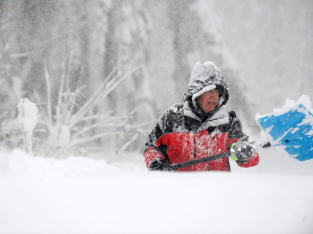 A person in a winter jacket actively shoveling snow during a snowfall, demonstrating snow removal services by Becker Landscape & Design in Woodbury, MN.