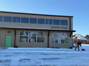 A person shoveling snow from a commercial building walkway, demonstrating snow removal by Greenhouse Outdoors in Springdale, AR.