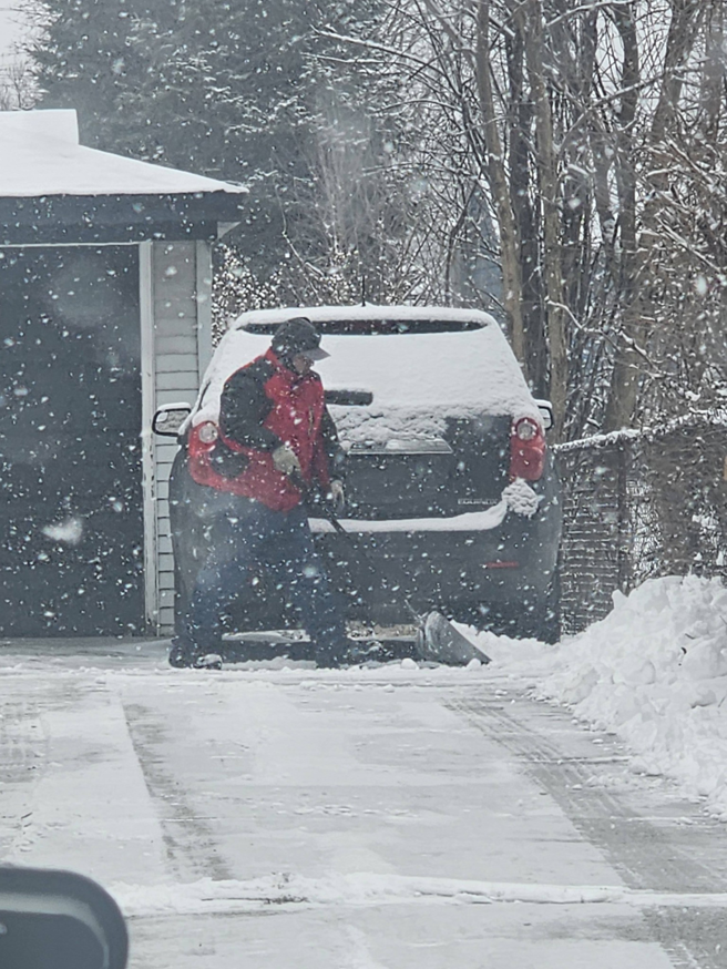 A person in a red jacket shoveling snow from a residential driveway, performed by Two brothers landscaping inc. in Fuquay Varina, NC.