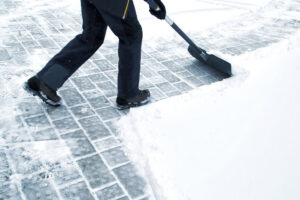 A person shoveling snow from a paved area, demonstrating manual snow removal services by JC Snow Management in Mount Vernon, NY