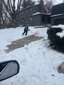 A person actively shoveling snow from a residential sidewalk by Jmccllm landscaping lawn care, junk removal in Springfield, IL.