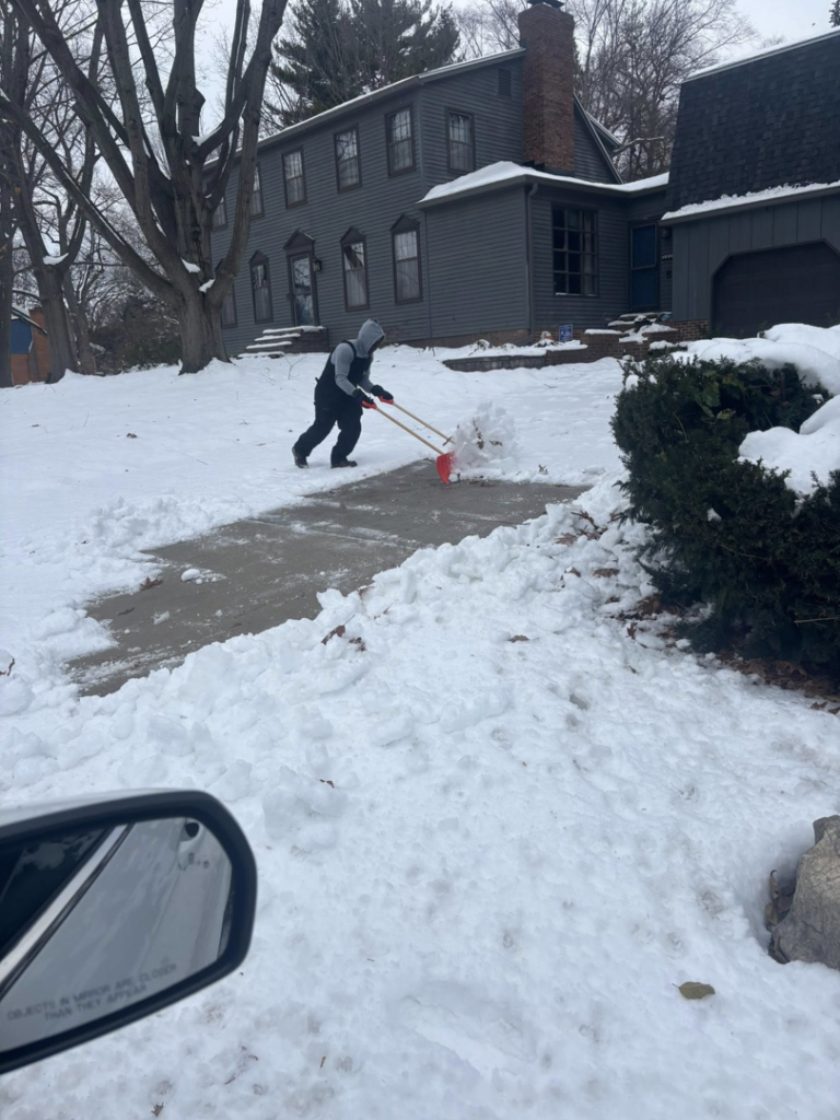 A person actively shoveling snow from a residential sidewalk by Jmccllm landscaping lawn care, junk removal in Springfield, IL.