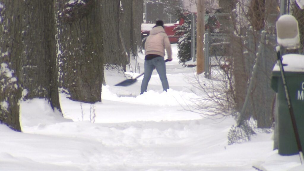 A person actively shoveling snow from a sidewalk, demonstrating snow removal services by QUIKPLOW in Grand Rapids, MI.