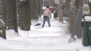 A person actively shoveling snow from a sidewalk, demonstrating snow removal services by QUIKPLOW in Grand Rapids, MI.