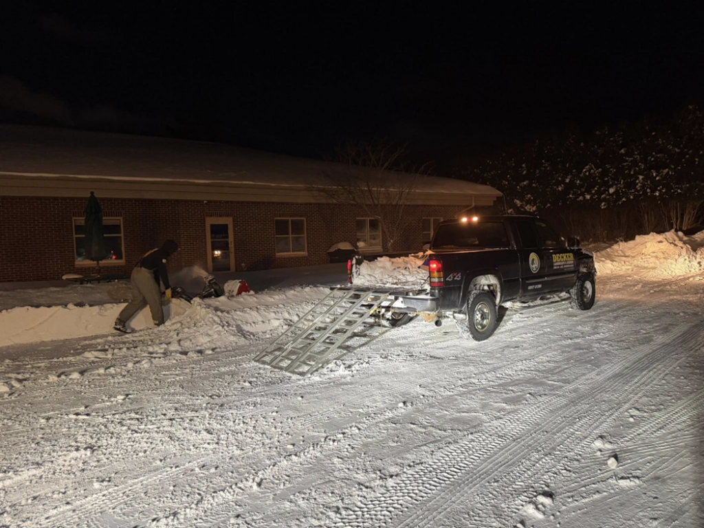 A person using a snow blower to clear a snowy driveway at night for Eric's Winter & Landscape Services in Appleton, WI