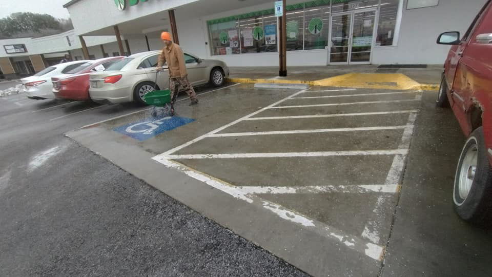 A person spreading ice melt in a commercial parking lot for snow removal by Kickin Grass Lawncare LLC in Springdale, AR.