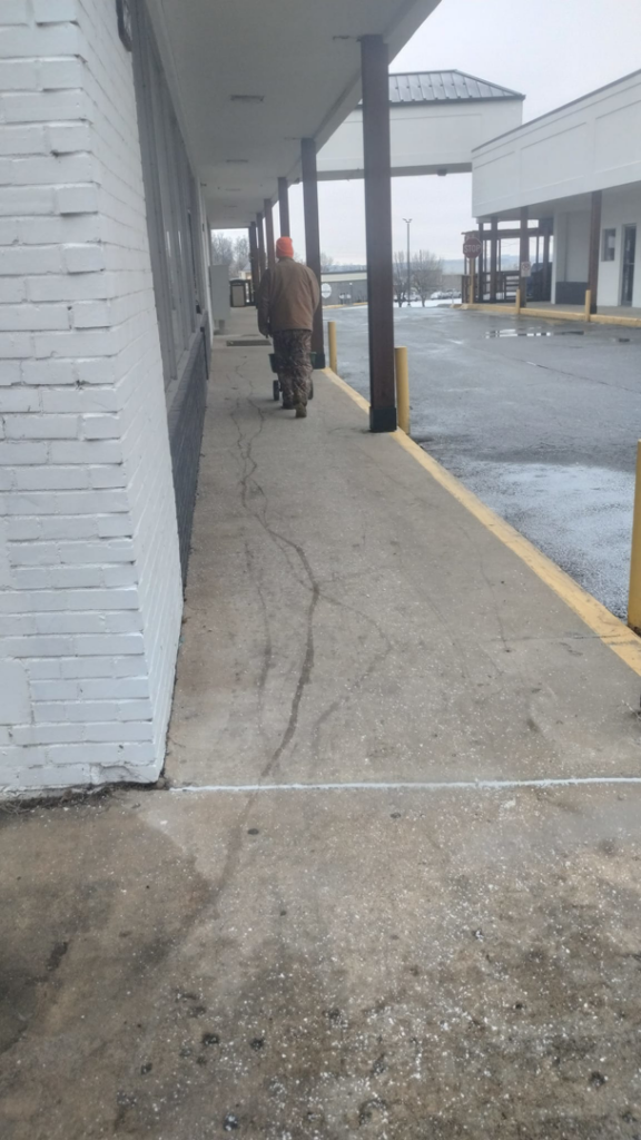 A person spreading ice melt on a commercial sidewalk for snow removal by Kickin Grass Lawncare LLC in Springdale, AR.