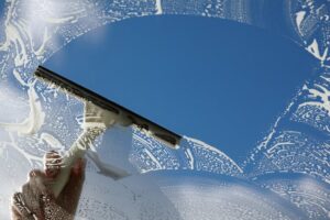 A person using a squeegee to clean a window with soap suds, showcasing window cleaning by Orange Cleaning Services in New Haven, CT
