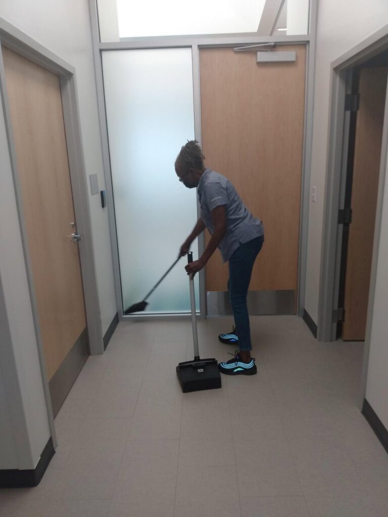 A cleaner sweeping a hallway with a broom and dustpan, performed by Janice Janitorial LLC in Baton Rouge, LA.