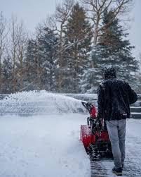 A person using a red snow blower to clear a snow-covered driveway for SA Mowing in Livonia, MI.