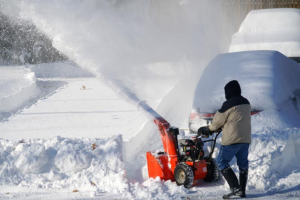 A person using a snow blower to clear a driveway of snow, a service provided by Snow Be Gone in Denver, CO
