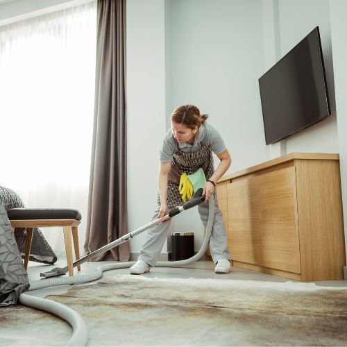 A professional cleaner from Cura Maids vacuuming a rug in a room in Raleigh, NC.