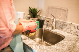 A person wearing pink gloves washing a mug in a kitchen sink, representing Two Maids of Hilton Head, SC.