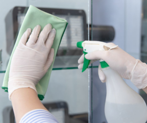 A person wearing gloves wiping a glass surface with a spray bottle and cloth at Orange Cleaning Services in New Haven, CT
