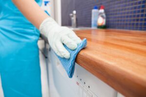 A person wearing gloves wiping a kitchen countertop with a blue cloth for Core Needs Janitorial in Indianapolis, IN.