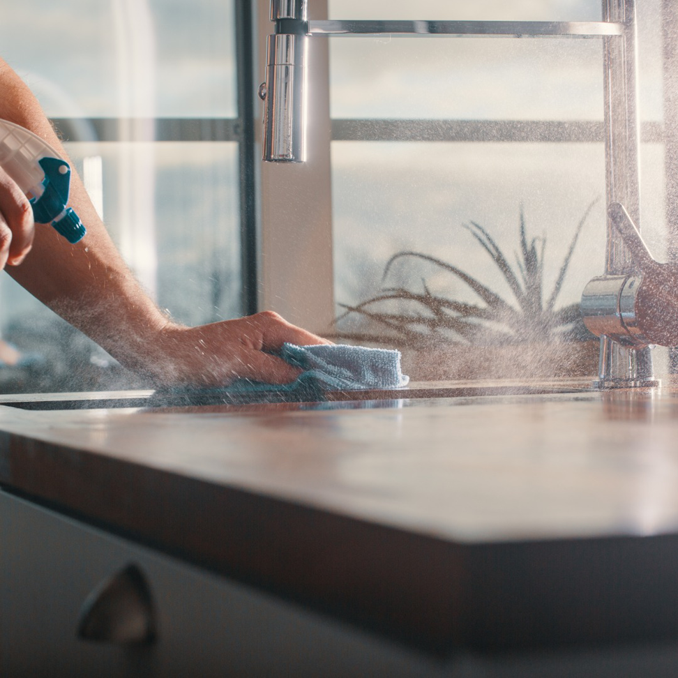A person spraying and wiping a kitchen countertop, demonstrating cleaning services by Phoenix Move Out House Cleaning Pros in Chandler, AZ