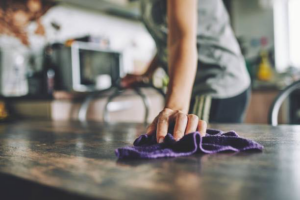 A person wiping a kitchen table with a cloth, demonstrating house cleaning services by Peak&co Cleaners in Great Falls, MT.