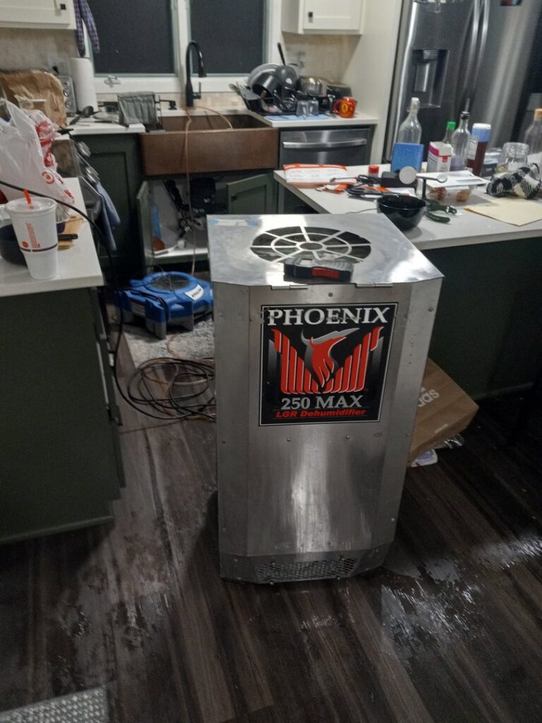 A Phoenix dehumidifier working on a wet kitchen floor during water damage restoration by Restoration Alliance Services in Elk River, MN.