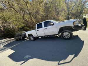 A white pickup tow truck from Jb's Towing & Recovery towing a dark sedan on a road in Rossville, GA.