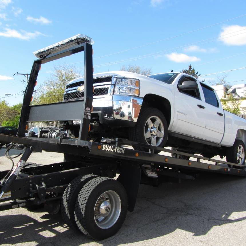 A white pickup truck being transported on a flatbed tow truck by Bakersfield Towing Company in Bakersfield, CA.