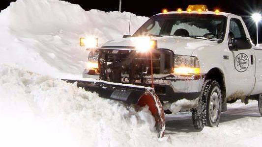 A white pickup truck with a snow plow actively clearing snow at night for Snow & Ice Management Company in Pittsburgh, PA.