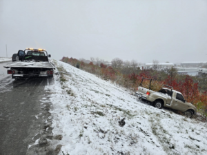 Montes Towing Services truck on a snowy road, preparing to recover a pickup truck from an embankment in Indianapolis, IN.