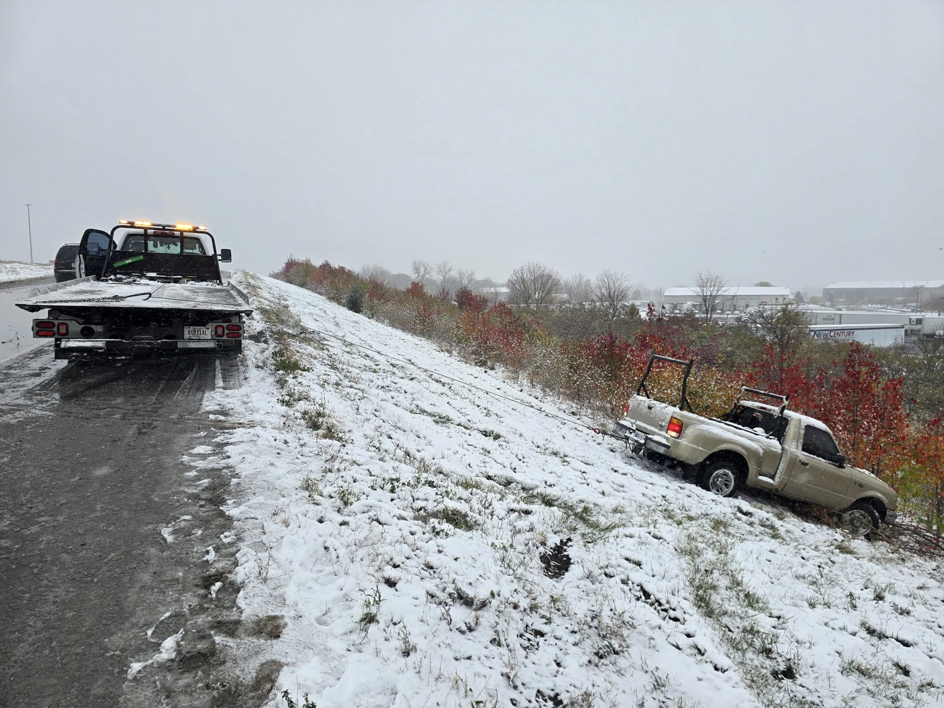 Montes Towing Services truck on a snowy road, preparing to recover a pickup truck from an embankment in Indianapolis, IN.