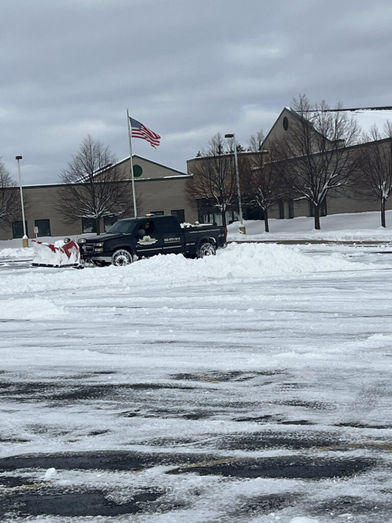 A pickup truck with a snow plow clearing a large parking lot, performed by Luna Landscape Pro in Racine, WI.