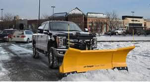 A black pickup truck equipped with a yellow snow plow ready for service by Royal Snow Removal in Gresham, OR.