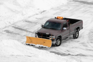 A pickup truck with a yellow snow plow clearing snow, demonstrating snow removal services by 3-D Lawncare & Landscaping in Flint, MI.
