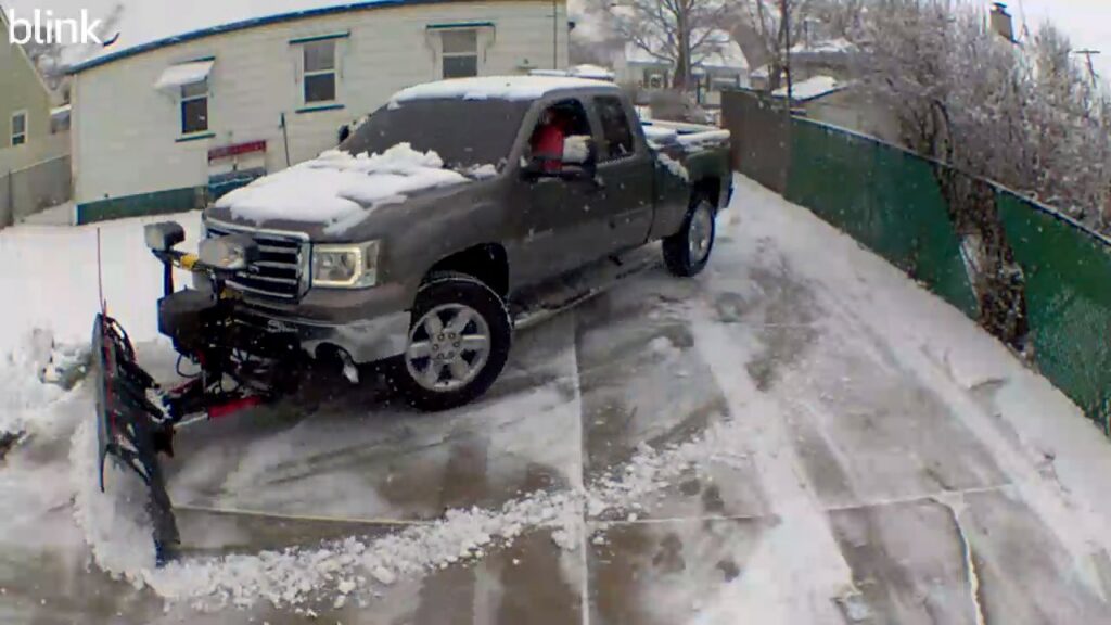 A pickup truck with a snow plow clearing a residential driveway for The Yard Guy LLC in Kenosha, WI
