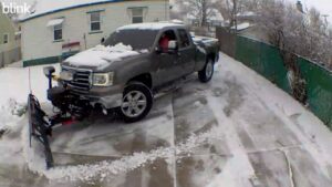 A pickup truck with a snow plow clearing a residential driveway for The Yard Guy LLC in Kenosha, WI