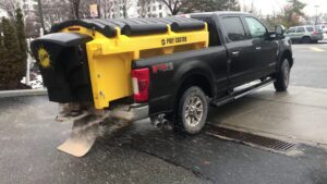 A pickup truck with a Poly Caster salt spreader actively spreading salt on a paved surface for JC Snow Management in Mount Vernon, NY