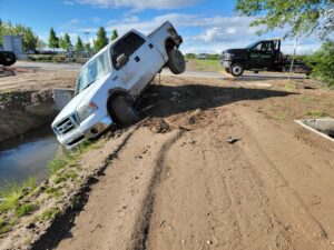 A white pickup truck stuck in a ditch, awaiting recovery by Gem State Towing and Recovery in Caldwell, ID.
