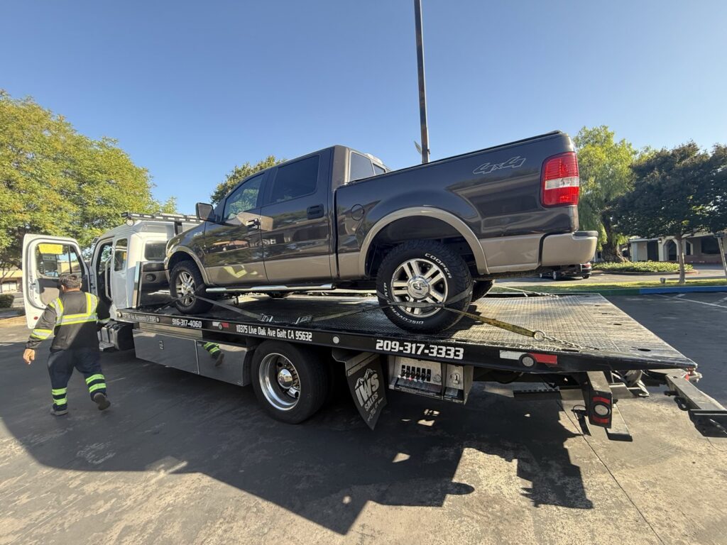 An AJ's Towing Services & Roadside Assistance flatbed tow truck loading a brown pickup truck in Sacramento, CA.
