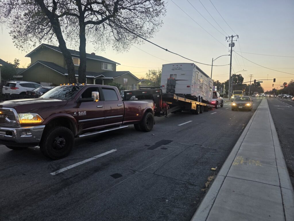 A heavy-duty pickup truck from Aguilar Towing towing a travel trailer on a street in San Jose, CA
