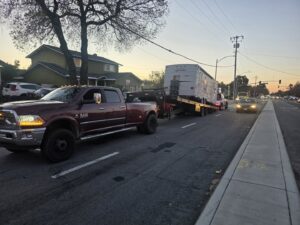 A heavy-duty pickup truck from Aguilar Towing towing a travel trailer on a street in San Jose, CA