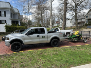 A pickup truck with a trailer carrying a riding lawn mower for Aj's Property Maintenance in Parkersburg, WV.