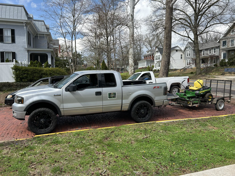 A pickup truck with a trailer carrying a riding lawn mower for Aj's Property Maintenance in Parkersburg, WV.
