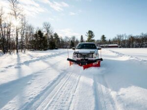 A pickup truck with a red snow plow actively clearing a wide, snow-covered road for PJs Full Service Contractors in Cleveland, OH.