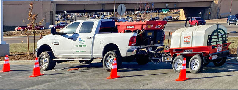A white pickup truck with a BOSS salt spreader and a liquid de-icing trailer, used for snow removal services by LAWN Sharks LLC in Colorado Springs, CO.