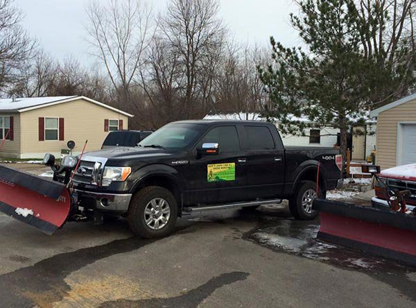 A black pickup truck equipped with a red snow plow, ready for snow removal services by Alex's lawn care in Rochester, MN.