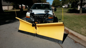 A white pickup truck with a yellow snow plow for professional snow removal by Tulsa snow removal by Kodiak Custom Masonry, Coweta, OK.
