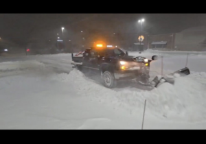 A snow plow truck actively clearing heavy snow from a road or parking lot at night for Eric's Winter & Landscape Services in Appleton, WI