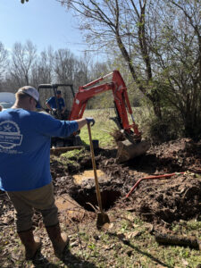 A plumber digging in a muddy trench to repair a burst pipe for Chris Dawson Plumbing LLC and Septic System Specialist in Athens, GA.