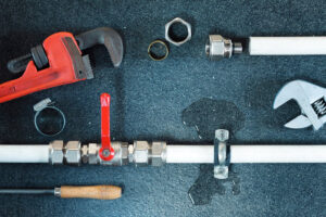 Plumbing leak repair with tools and visible water damage by Clog Busterz Plumbing Services in Richmond, KY.