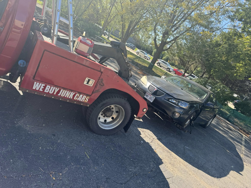 A PNB towing truck hauling a damaged dark sedan from a parking lot in Madison, WI.